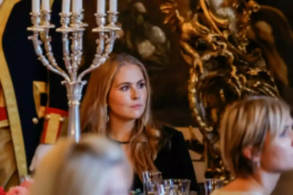 La princesa Amalia sentada en una mesa elegante durante un evento formal con candelabro plateado y decoración dorada al fondo. La princesa Amalia sentada en una mesa elegante durante un evento formal con candelabro plateado y decoración dorada al fondo.
