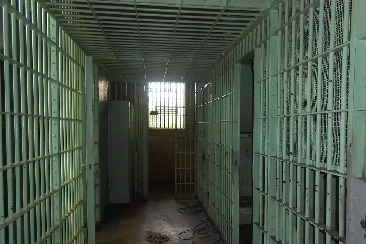 Narrow hallway of a prison with cells with green bars and a window at the end letting in natural light Narrow hallway of a prison with cells with green bars and a window at the end letting in natural light