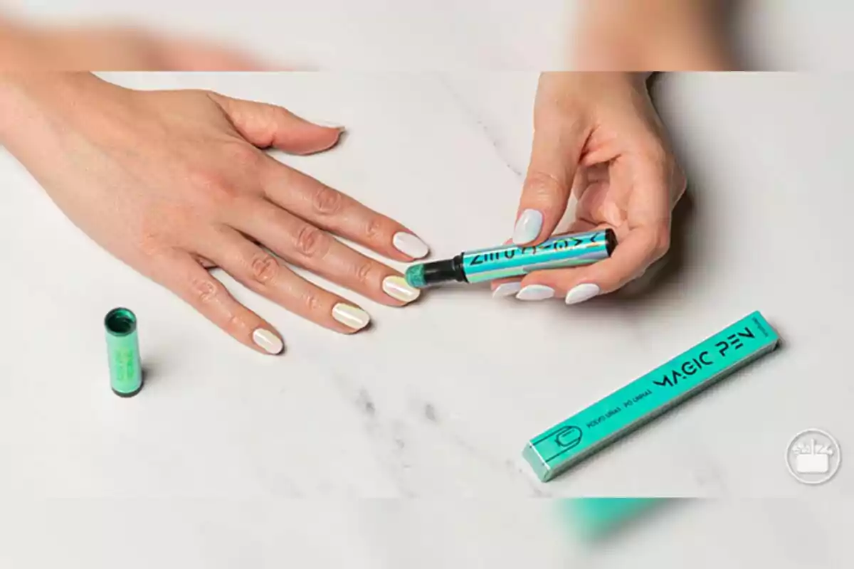 Mano aplicando un rotulador corrector de esmalte de uñas de Mercadona sobre las uñas pintadas de color claro sobre una superficie blanca. Mano aplicando un rotulador corrector de esmalte de uñas de Mercadona sobre las uñas pintadas de color claro sobre una superficie blanca.