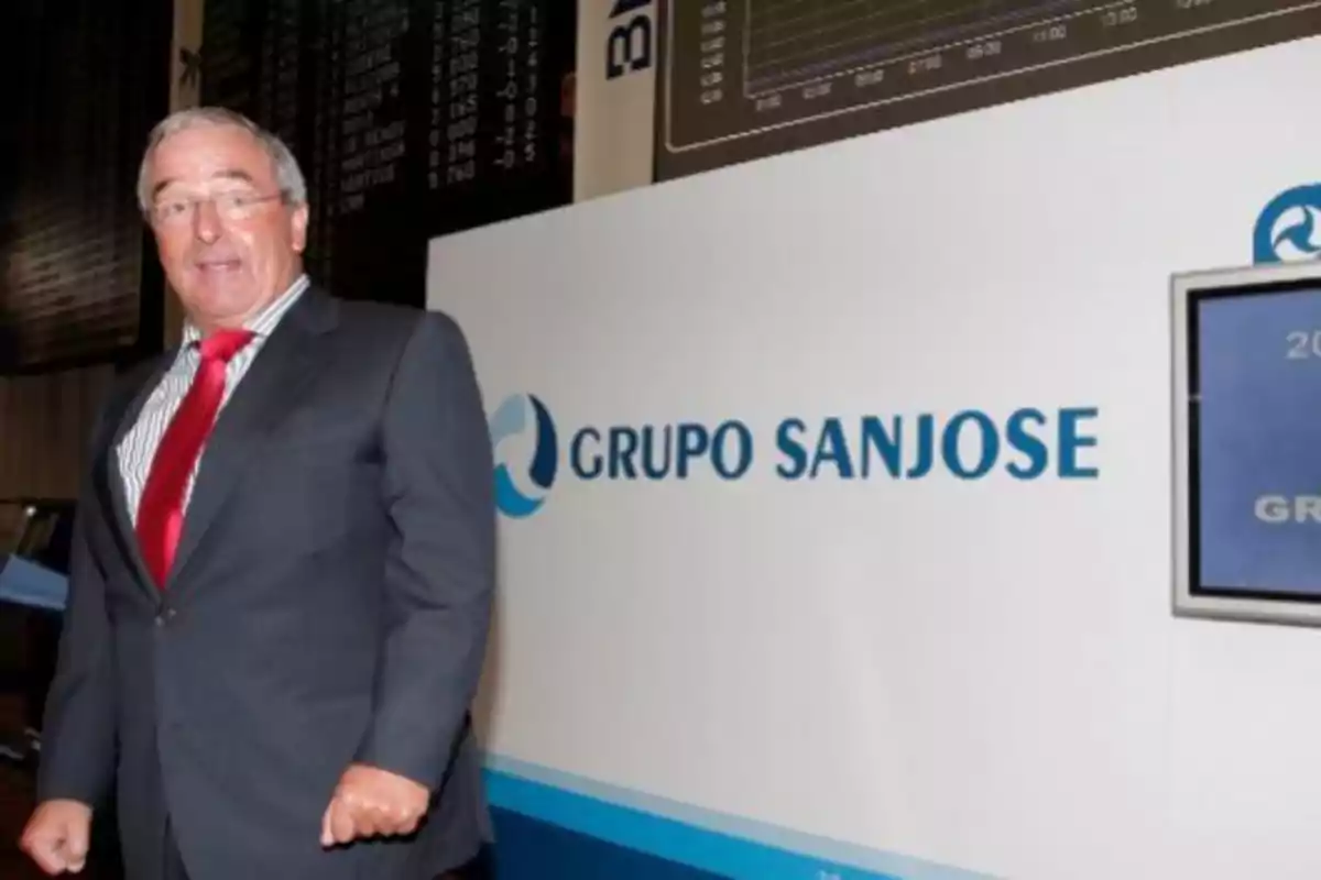 Hombre de traje y corbata roja posando junto a un cartel de Grupo Sanjose