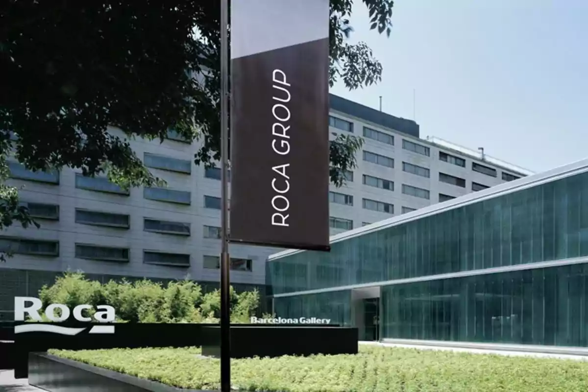 Edificio moderno con fachada de vidrio y un letrero que dice Roca Group junto a un jardín y vegetación