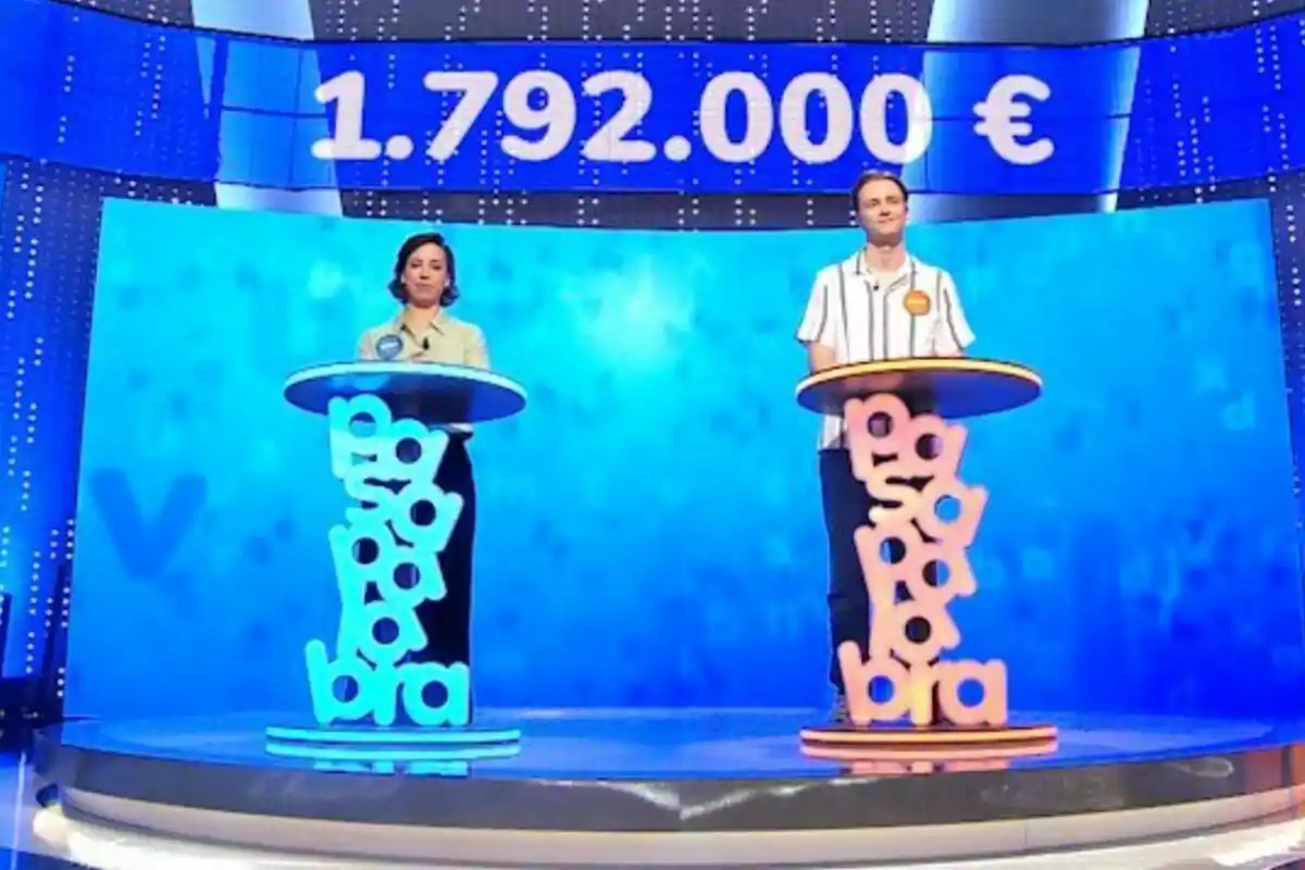 Dos concursantes de pie en un plató de televisión con atriles coloridos -que son Rosa y Manu- y una pantalla al fondo que muestra un premio de un millón setecientos noventa y dos mil euros. Dos concursantes de pie en un plató de televisión con atriles coloridos -que son Rosa y Manu- y una pantalla al fondo que muestra un premio de un millón setecientos noventa y dos mil euros.