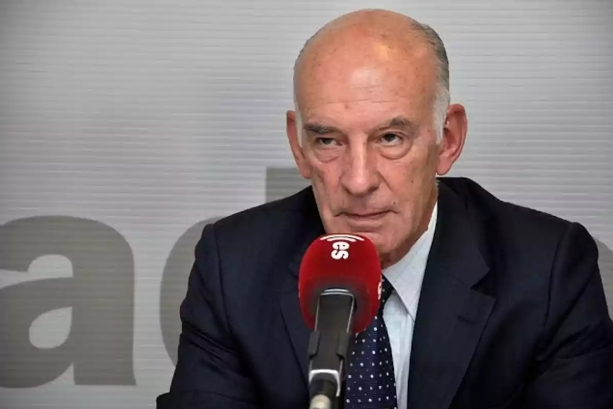 Hombre mayor de traje oscuro hablando frente a un micrófono rojo en un estudio de radio Hombre mayor de traje oscuro hablando frente a un micrófono rojo en un estudio de radio