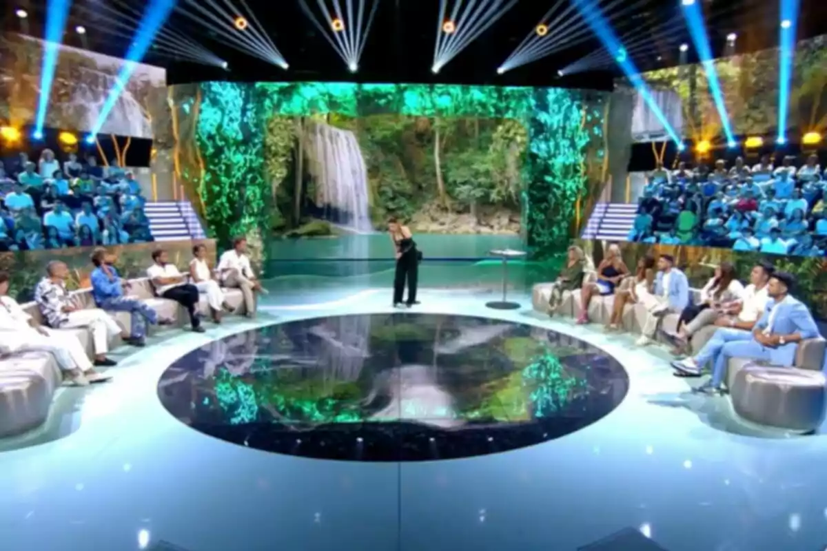 Un plató de televisión con público y participantes sentados en sofás, una presentadora de pie en el centro y una gran pantalla al fondo mostrando una cascada rodeada de vegetación. Captura de 'Supervivientes' Un plató de televisión con público y participantes sentados en sofás, una presentadora de pie en el centro y una gran pantalla al fondo mostrando una cascada rodeada de vegetación. Captura de 'Supervivientes'