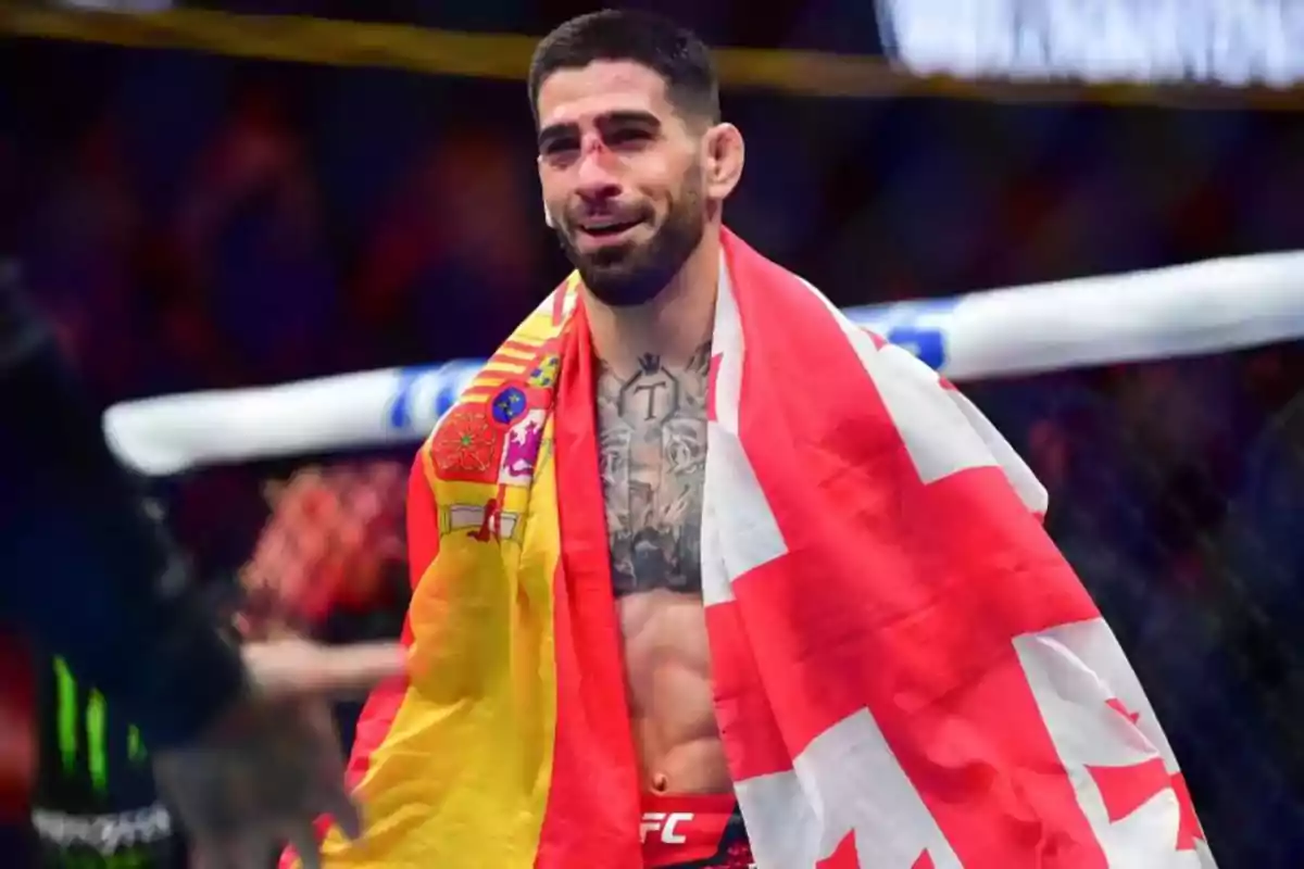 Un luchador de artes marciales mixtas sonríe dentro del octágono con la bandera de España y otra bandera roja y blanca sobre los hombros Un luchador de artes marciales mixtas sonríe dentro del octágono con la bandera de España y otra bandera roja y blanca sobre los hombros
