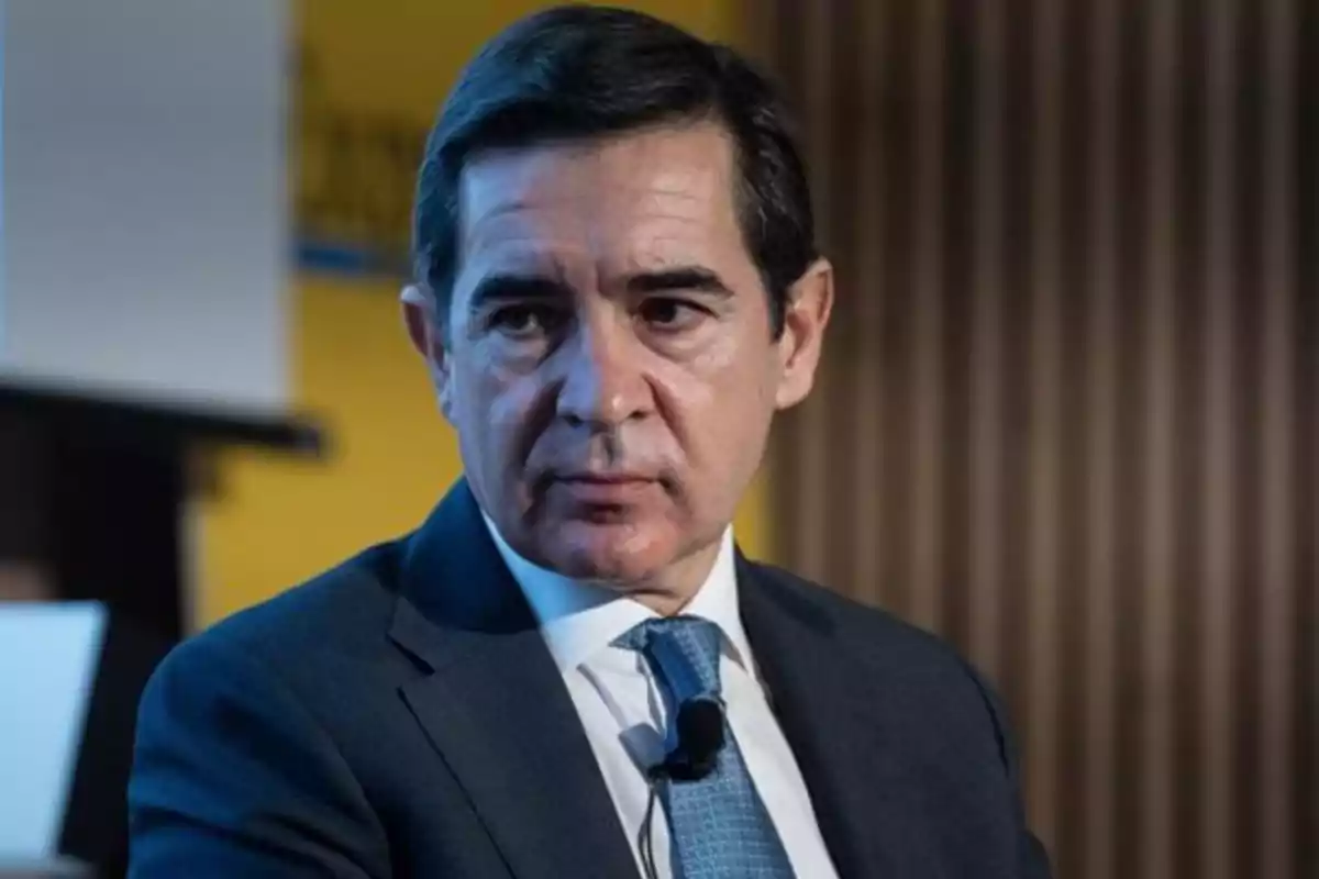 Hombre de cabello oscuro con traje y corbata azul sentado en un entorno profesional