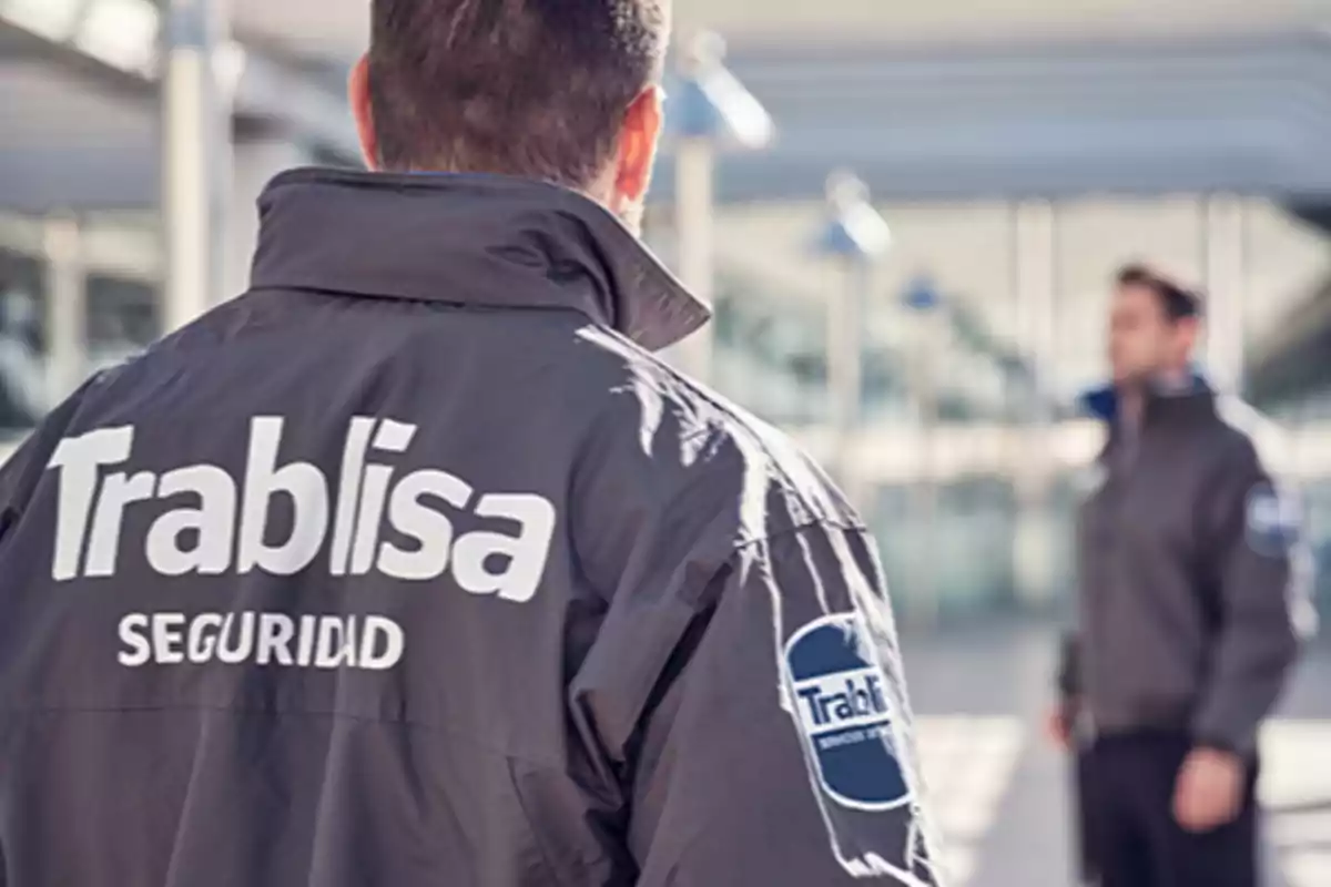 Persona de espaldas con chaqueta de seguridad de la empresa Trablisa en un entorno moderno y luminoso Persona de espaldas con chaqueta de seguridad de la empresa Trablisa en un entorno moderno y luminoso