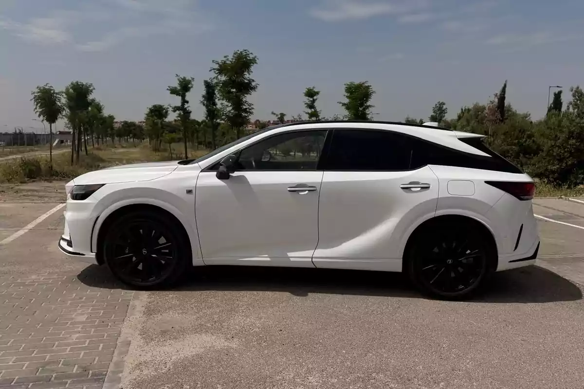 Auto blanco moderno estacionado en un lugar al aire libre con árboles y cielo parcialmente nublado al fondo Auto blanco moderno estacionado en un lugar al aire libre con árboles y cielo parcialmente nublado al fondo
