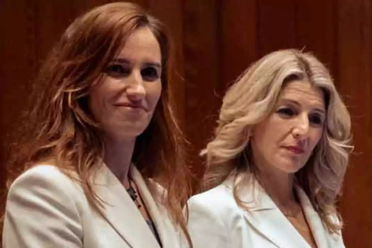 Dos mujeres con chaquetas blancas posan frente a un fondo de madera