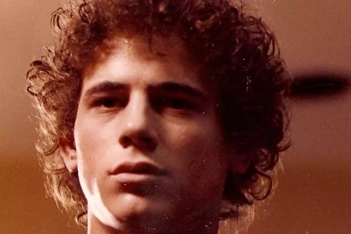 Primer plano de un joven con cabello rizado y expresión seria en un ambiente interior iluminado. Primer plano de un joven con cabello rizado y expresión seria en un ambiente interior iluminado.