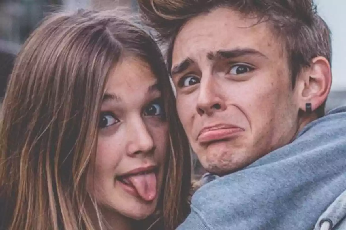 Dos jóvenes hacen caras graciosas mirando a la cámara, una chica saca la lengua y un chico pone una expresión exagerada de sorpresa. Dos jóvenes hacen caras graciosas mirando a la cámara, una chica saca la lengua y un chico pone una expresión exagerada de sorpresa.