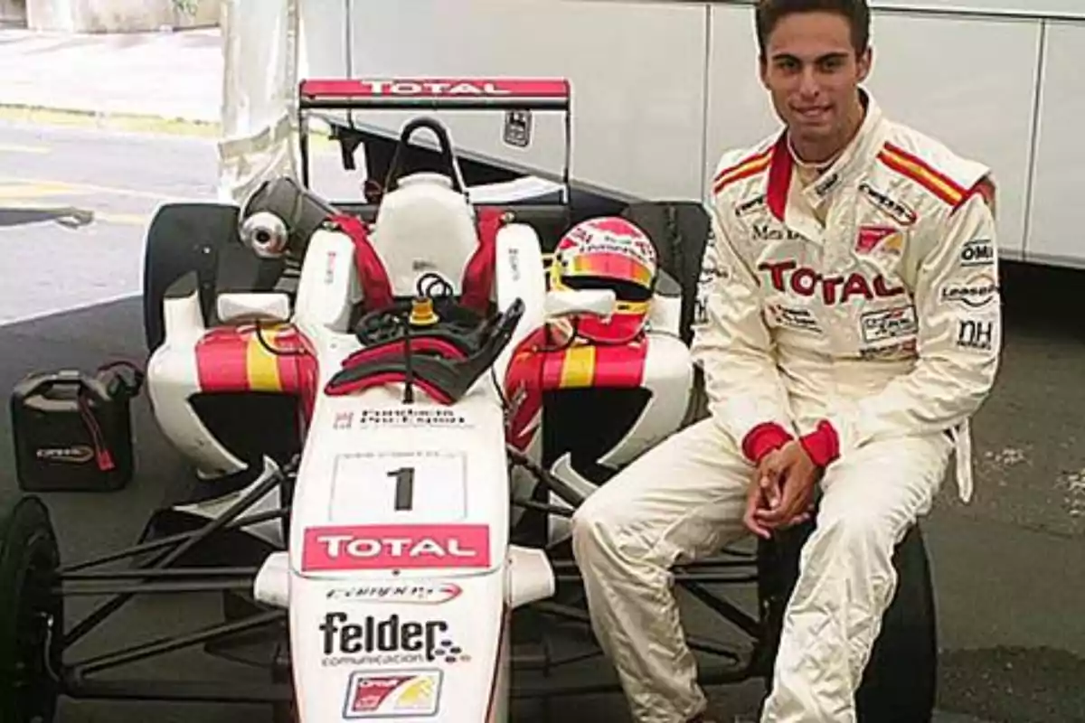 Piloto de automovilismo con traje blanco de carreras sentado junto a un monoplaza de competición decorado con los colores y logotipos de la marca Total Piloto de automovilismo con traje blanco de carreras sentado junto a un monoplaza de competición decorado con los colores y logotipos de la marca Total