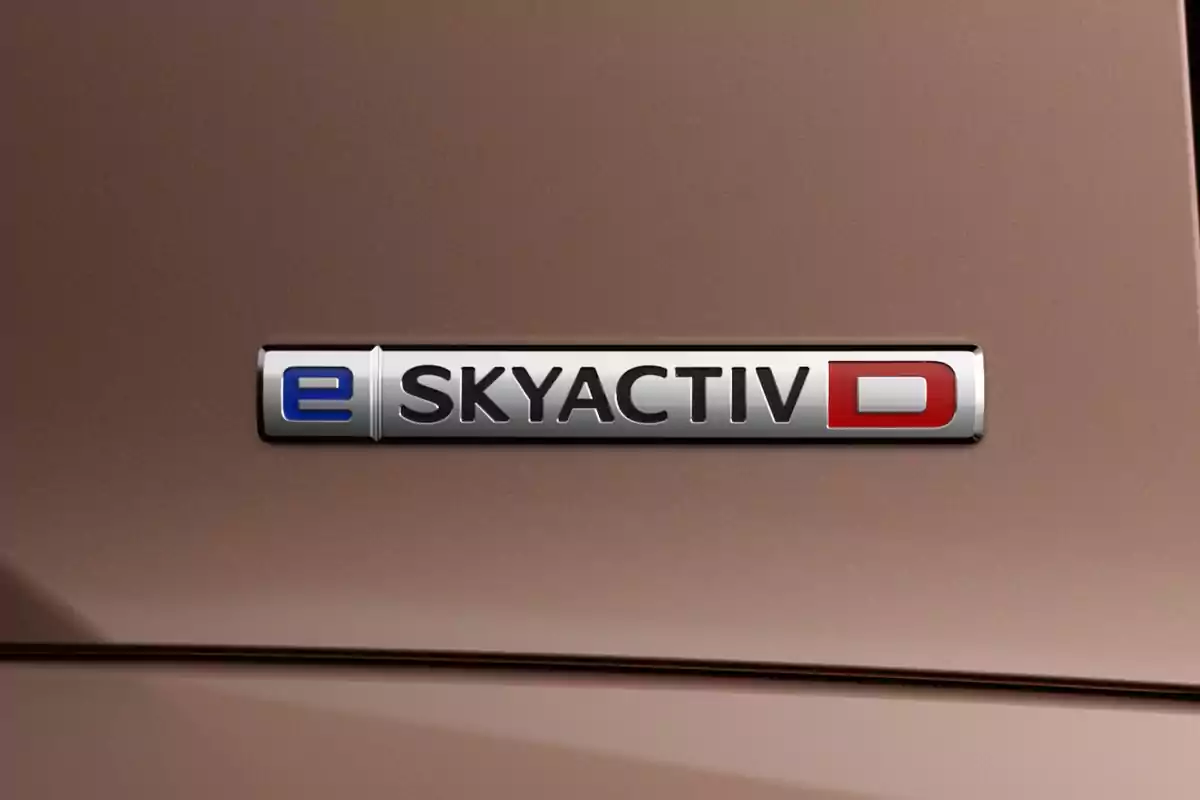 Emblema metálico de Mazda con la inscripción e-SKYACTIV D sobre una carrocería color marrón Emblema metálico de Mazda con la inscripción e-SKYACTIV D sobre una carrocería color marrón