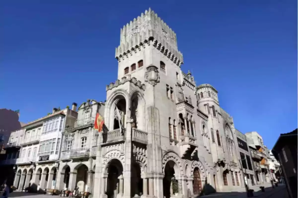 Edificio histórico de piedra con arquitectura medieval y una torre central en una plaza urbana bajo un cielo despejado Edificio histórico de piedra con arquitectura medieval y una torre central en una plaza urbana bajo un cielo despejado