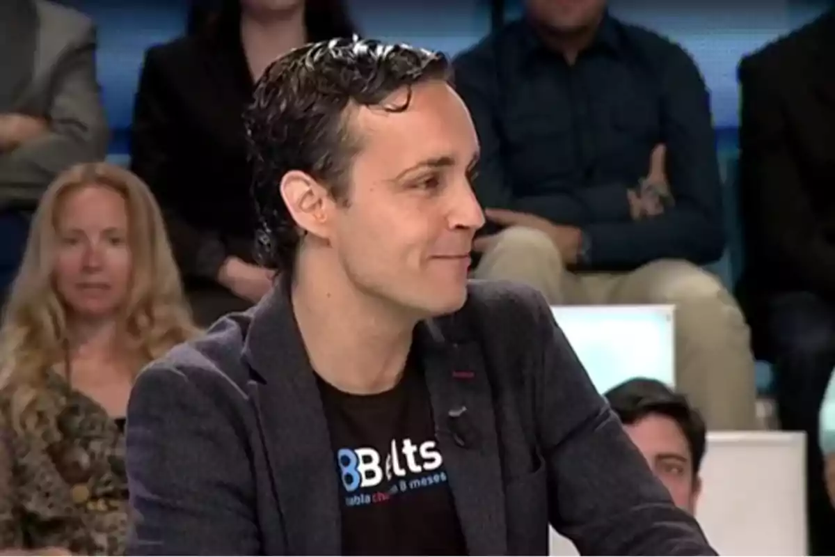 Hombre de cabello oscuro con chaqueta y camiseta negra participando en un programa de televisión con público al fondo Hombre de cabello oscuro con chaqueta y camiseta negra participando en un programa de televisión con público al fondo