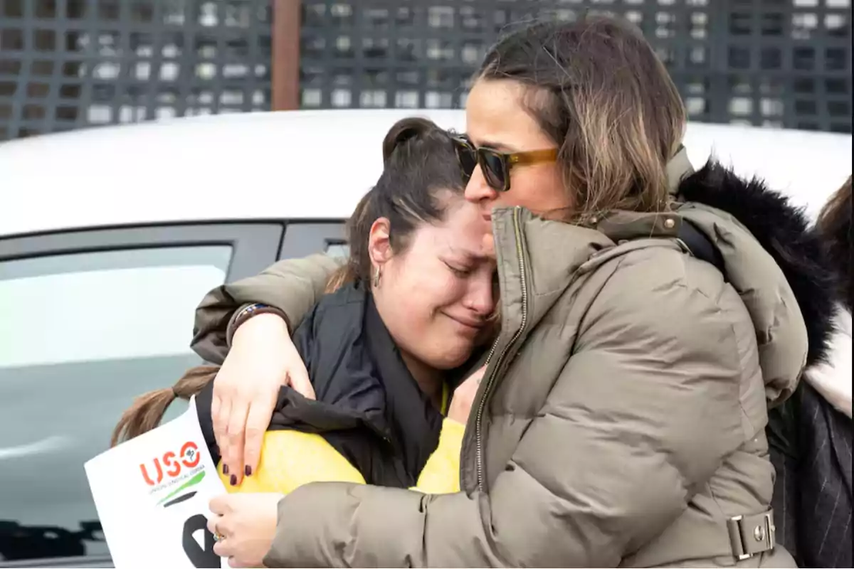 Dos mujeres se abrazan mientras una de ellas llora y la otra la consuela con un beso en la cabeza Dos mujeres se abrazan mientras una de ellas llora y la otra la consuela con un beso en la cabeza