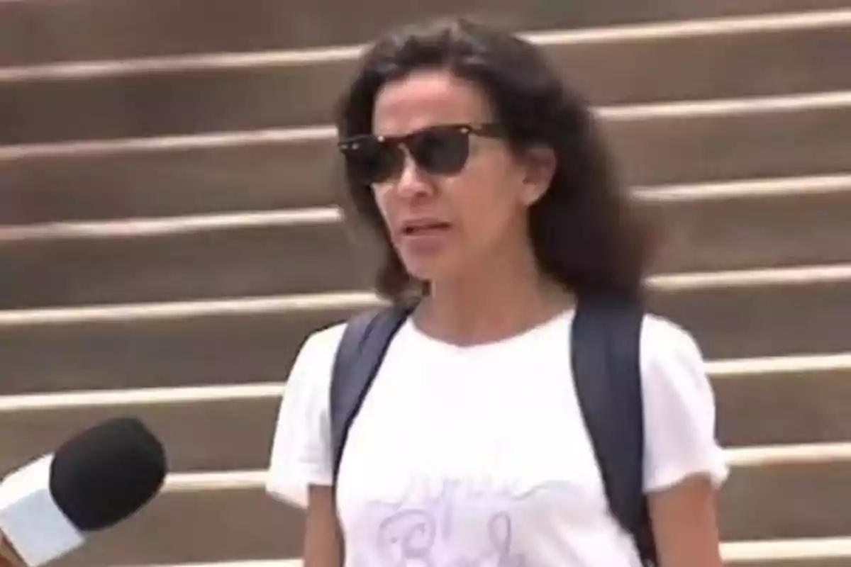 Mujer con gafas de sol y mochila caminando frente a unas escaleras mientras un micrófono se acerca a ella Mujer con gafas de sol y mochila caminando frente a unas escaleras mientras un micrófono se acerca a ella