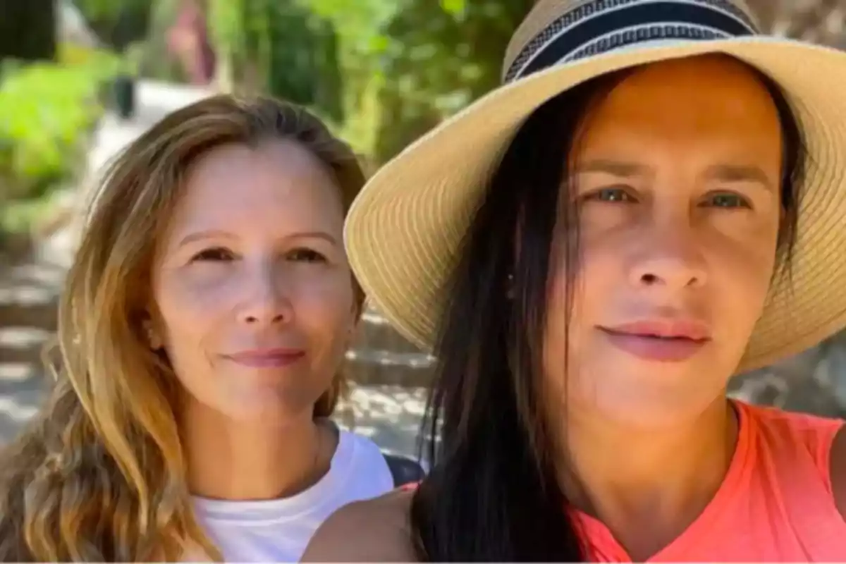 Dos mujeres posan para una selfie al aire libre, una de ellas lleva sombrero y la otra tiene el cabello suelto, ambas sonríen levemente y el fondo muestra un camino rodeado de vegetación. Dos mujeres posan para una selfie al aire libre, una de ellas lleva sombrero y la otra tiene el cabello suelto, ambas sonríen levemente y el fondo muestra un camino rodeado de vegetación.
