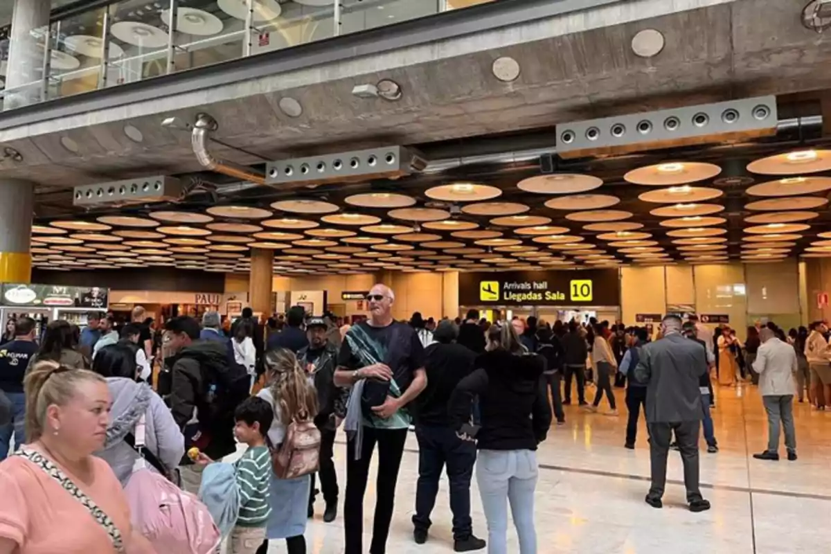 Personas esperando en la zona de llegadas de un aeropuerto concurrido con un letrero amarillo que indica la sala 10 Personas esperando en la zona de llegadas de un aeropuerto concurrido con un letrero amarillo que indica la sala 10