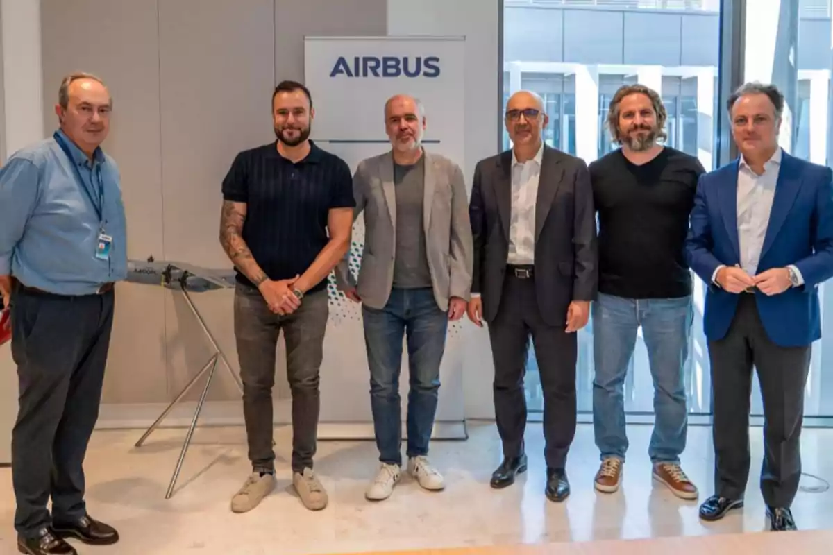 Seis hombres posan juntos en una oficina moderna frente a un cartel de Airbus Seis hombres posan juntos en una oficina moderna frente a un cartel de Airbus