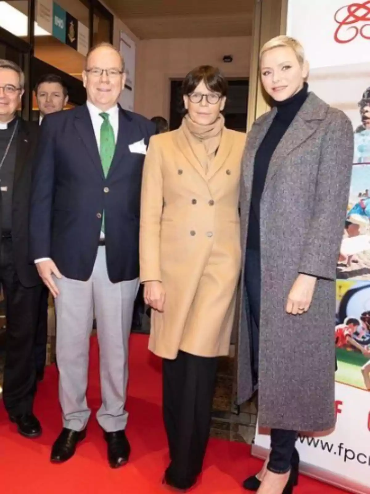 Tres personas posan sobre una alfombra roja en un evento formal, dos mujeres y un hombre, todos vestidos elegantemente y sonriendo a la cámara