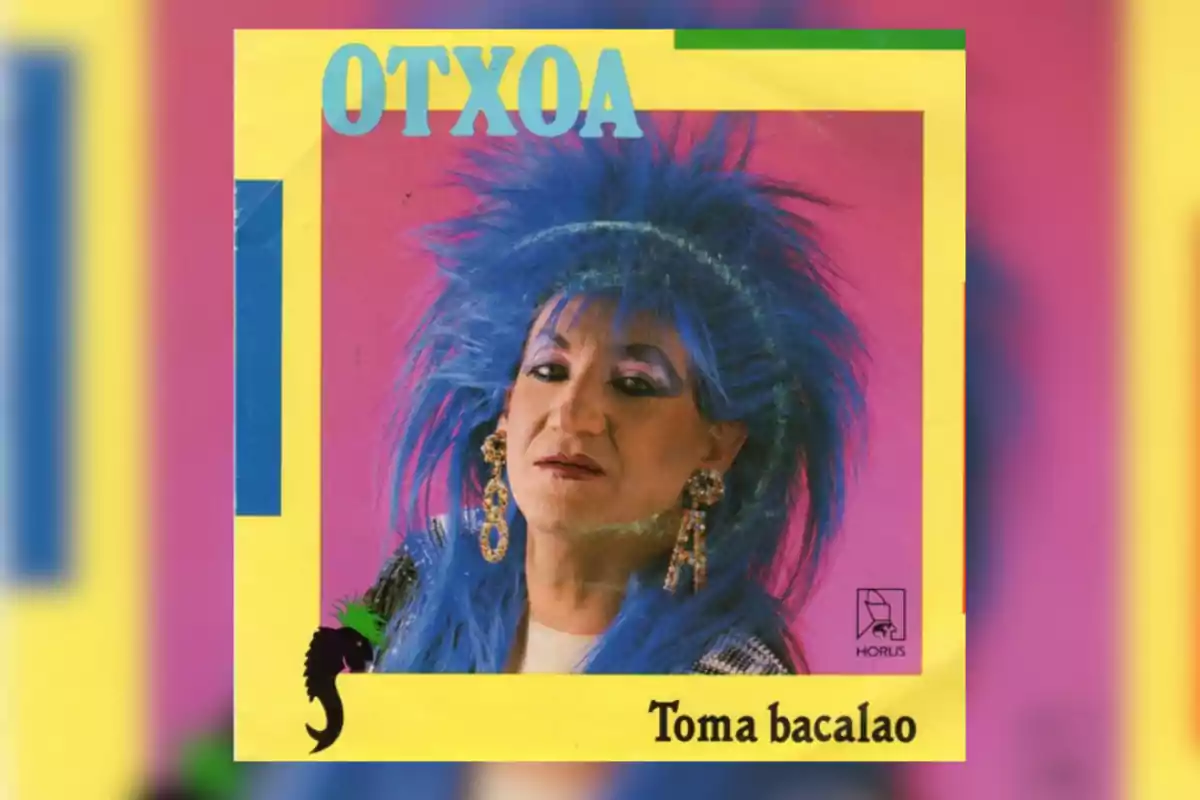 Portada de un disco con una persona de cabello azul y maquillaje llamativo sobre un fondo rosa, con el nombre Otxoa en la parte superior y el título Toma bacalao en la parte inferior Portada de un disco con una persona de cabello azul y maquillaje llamativo sobre un fondo rosa, con el nombre Otxoa en la parte superior y el título Toma bacalao en la parte inferior