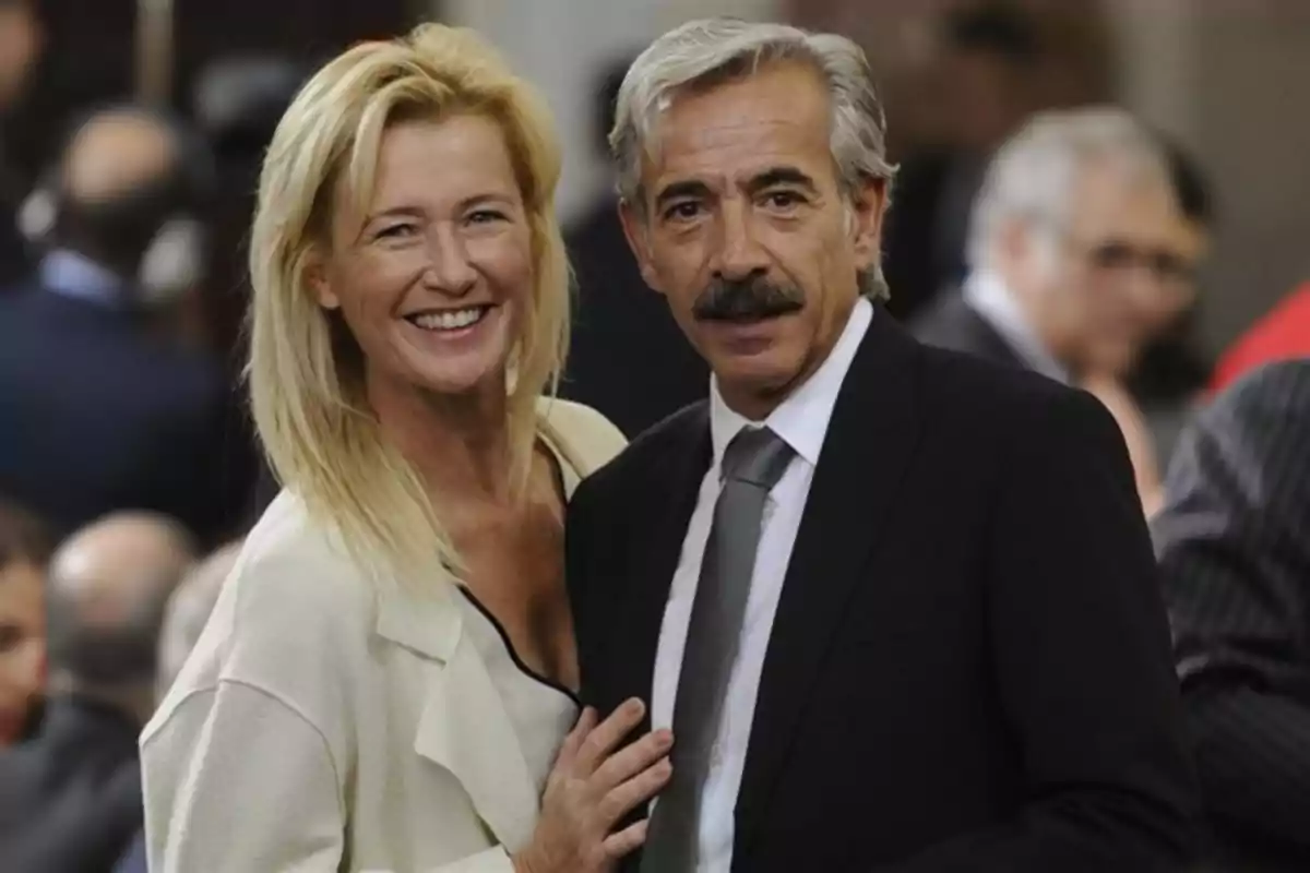 Pareja sonriente posando elegantemente en un evento formal con personas al fondo desenfocadas