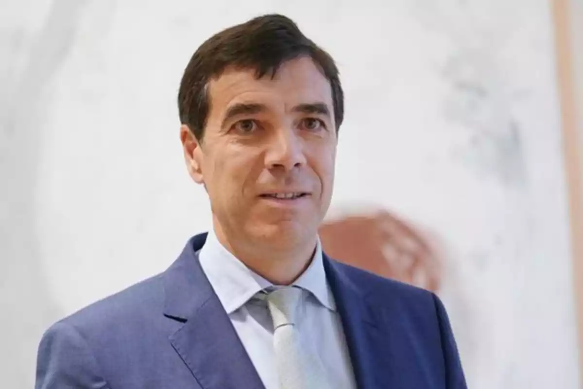 Hombre de cabello oscuro con traje azul y corbata clara posando frente a un fondo desenfocado. Hombre de cabello oscuro con traje azul y corbata clara posando frente a un fondo desenfocado.