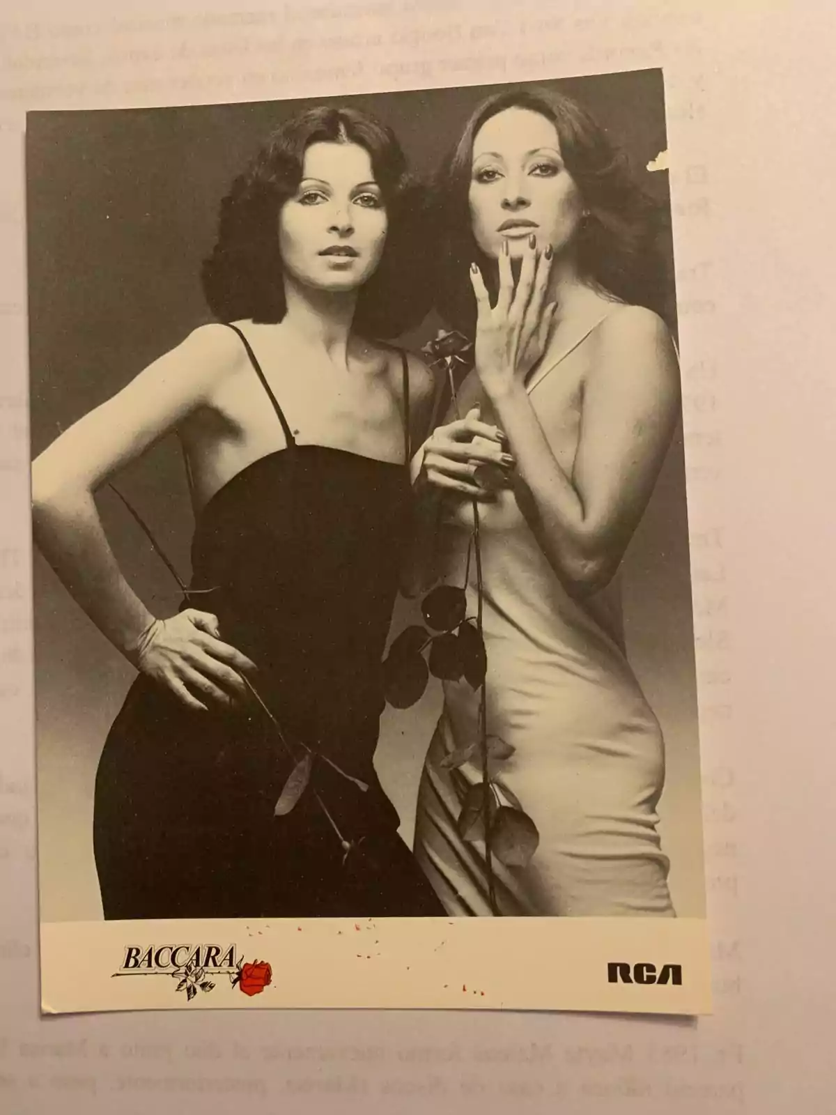Fotografía en blanco y negro de dos mujeres posando elegantemente, una con vestido negro y la otra con vestido claro, ambas sosteniendo una rosa Fotografía en blanco y negro de dos mujeres posando elegantemente, una con vestido negro y la otra con vestido claro, ambas sosteniendo una rosa