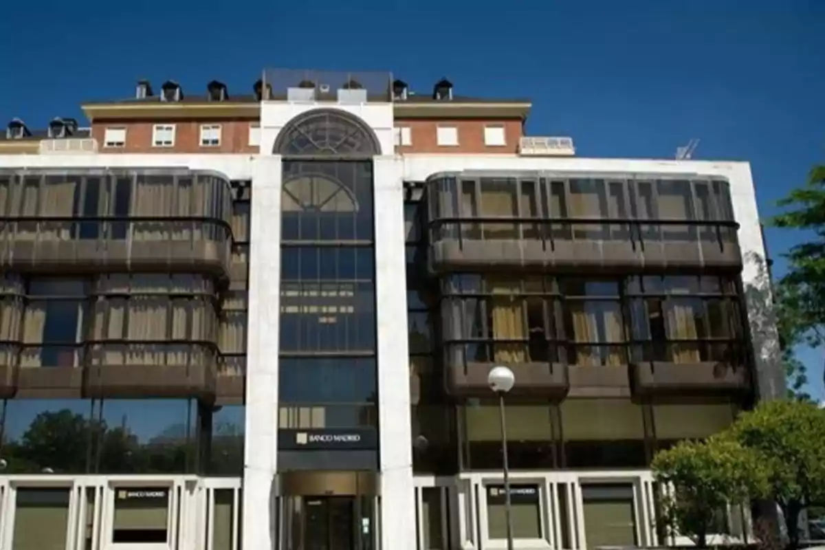 Fachada de un edificio moderno con ventanales oscuros y letreros de Banco Madrid en la entrada Fachada de un edificio moderno con ventanales oscuros y letreros de Banco Madrid en la entrada