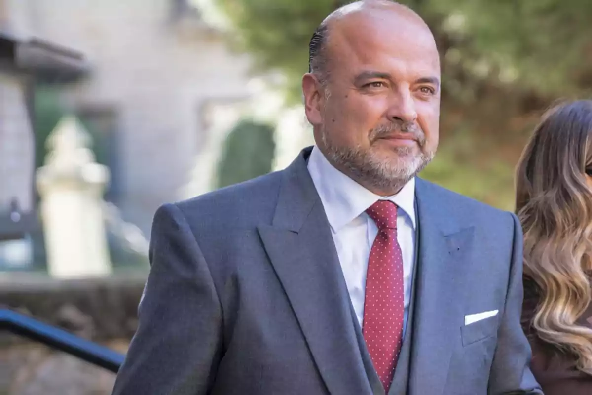 Hombre de mediana edad con barba y traje gris con corbata roja de puntos blancos en un entorno al aire libre Hombre de mediana edad con barba y traje gris con corbata roja de puntos blancos en un entorno al aire libre
