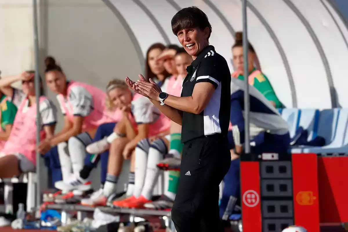 Entrenadora de fútbol animando a su equipo desde la banda mientras las jugadoras están sentadas en el banquillo Entrenadora de fútbol animando a su equipo desde la banda mientras las jugadoras están sentadas en el banquillo