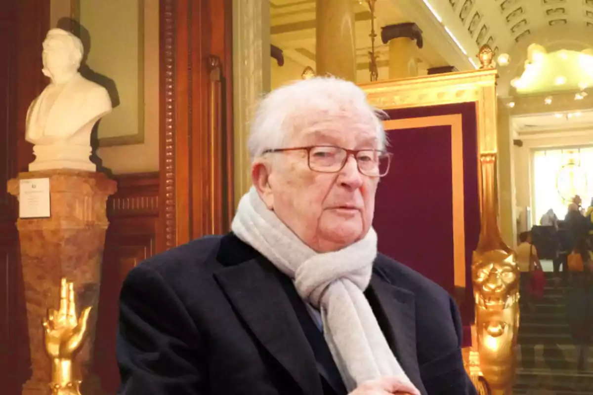 Hombre mayor con gafas y bufanda gris en un elegante interior con esculturas y detalles dorados