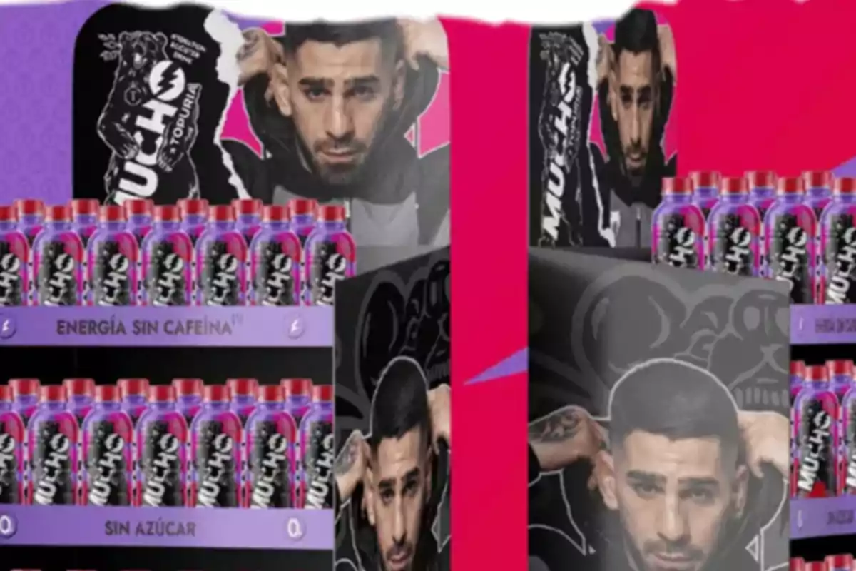 Bebidas energéticas en botellas con etiquetas negras y moradas exhibidas en un estante promocional con la imagen de un hombre de cabello corto y barba en el fondo Bebidas energéticas en botellas con etiquetas negras y moradas exhibidas en un estante promocional con la imagen de un hombre de cabello corto y barba en el fondo