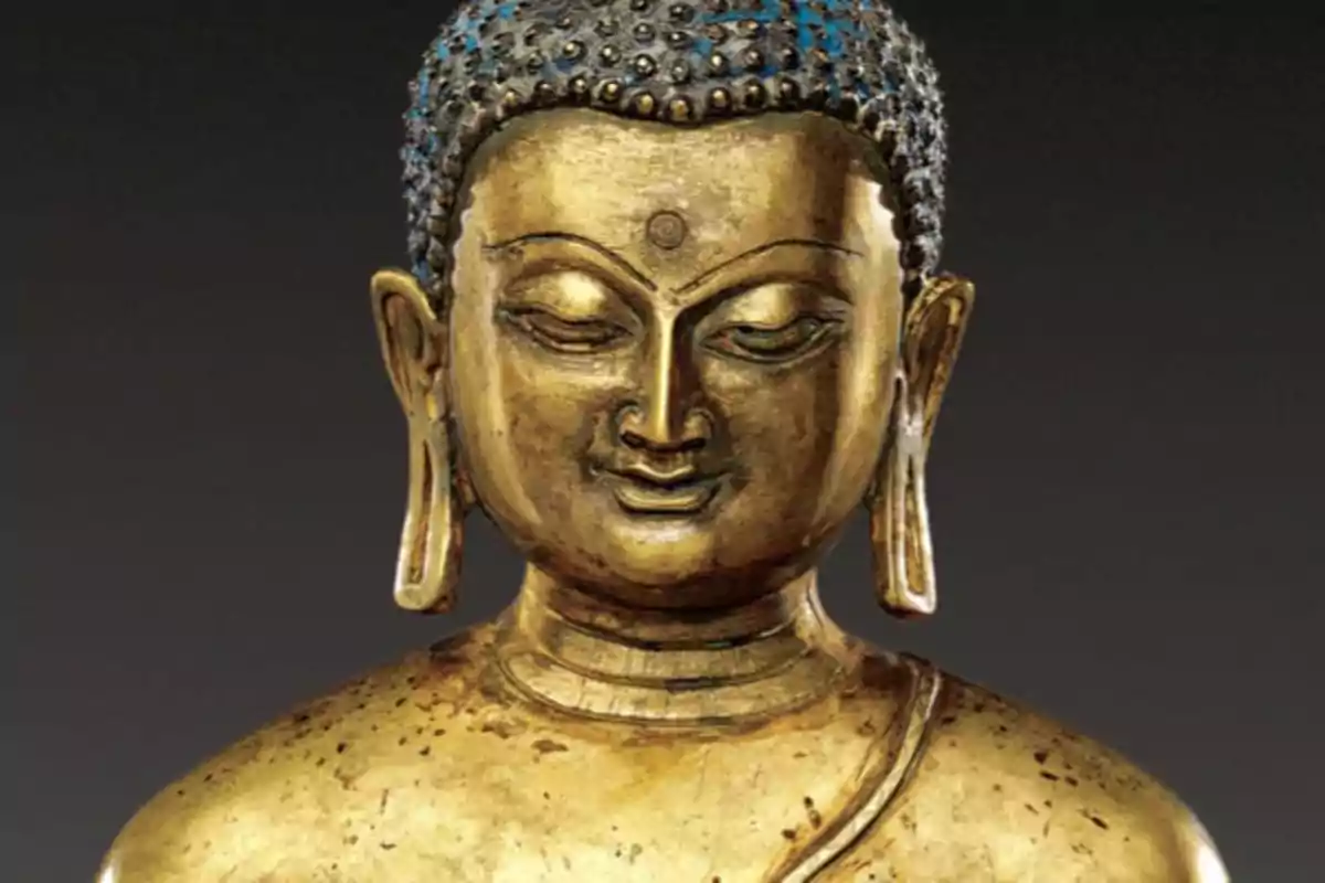 Escultura dorada de Buda con expresión serena y ojos cerrados sobre fondo oscuro
