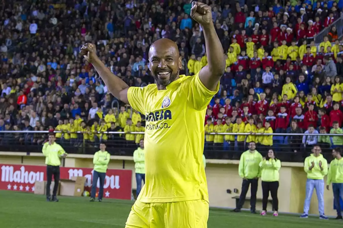 Futbolista sonriente con uniforme amarillo celebrando en un estadio lleno de aficionados Futbolista sonriente con uniforme amarillo celebrando en un estadio lleno de aficionados