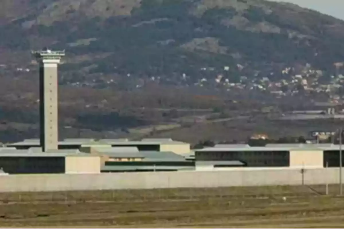 Vista exterior de una prisión de alta seguridad con una torre de vigilancia y montañas al fondo