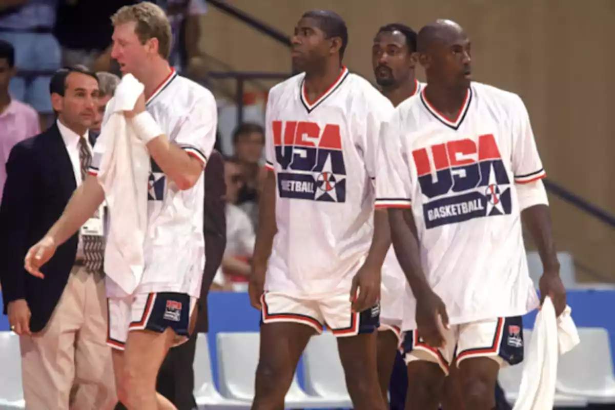 Jugadores de baloncesto del equipo de Estados Unidos caminando en la cancha durante un partido, usando uniformes blancos con el logo de USA Basketball Jugadores de baloncesto del equipo de Estados Unidos caminando en la cancha durante un partido, usando uniformes blancos con el logo de USA Basketball