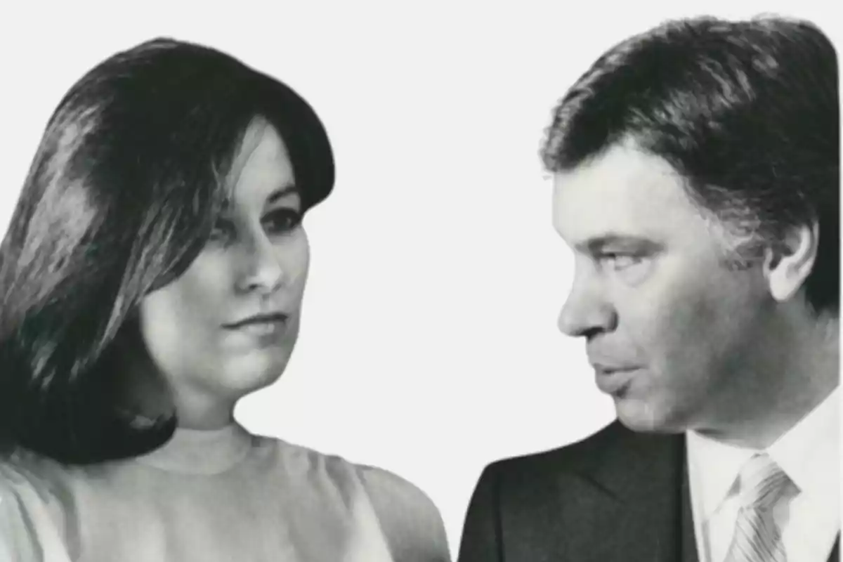 Fotografía en blanco y negro de una mujer y un hombre mirando hacia el frente, ambos con expresión seria y fondo blanco Fotografía en blanco y negro de una mujer y un hombre mirando hacia el frente, ambos con expresión seria y fondo blanco