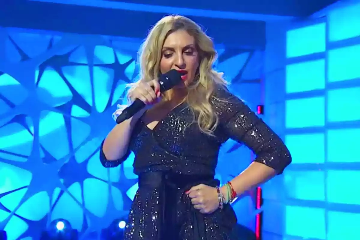 Mujer rubia con vestido negro brillante cantando en un escenario iluminado con luces azules Mujer rubia con vestido negro brillante cantando en un escenario iluminado con luces azules