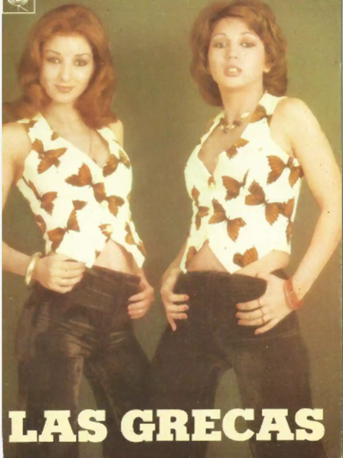 Dos mujeres posan juntas usando blusas blancas con estampado de mariposas y pantalones oscuros con el texto Las Grecas en la parte inferior Dos mujeres posan juntas usando blusas blancas con estampado de mariposas y pantalones oscuros con el texto Las Grecas en la parte inferior