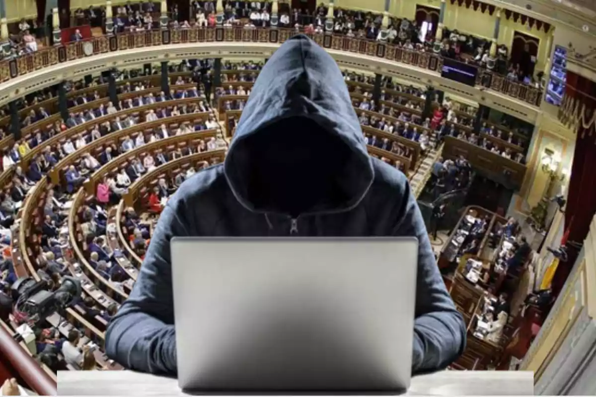 Persona encapuchada usando una computadora portátil frente a un parlamento lleno de gente