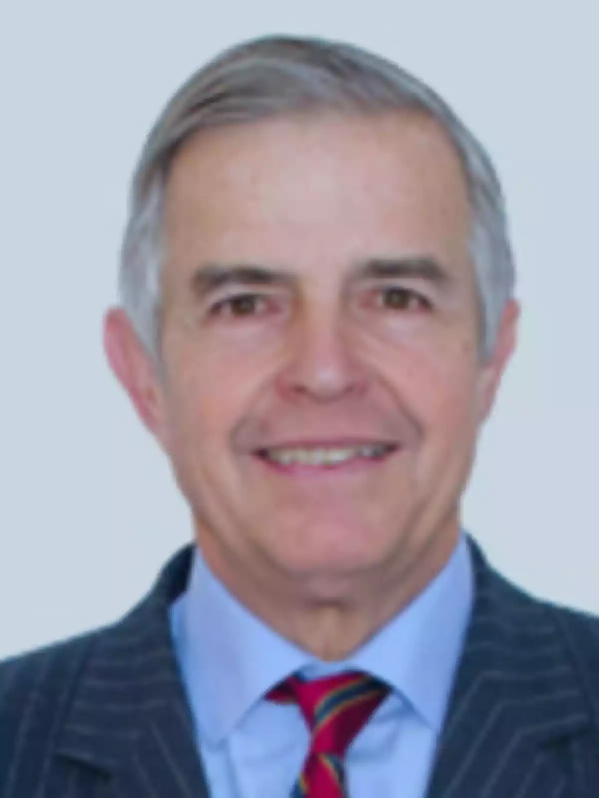 Hombre mayor de cabello canoso con traje a rayas y corbata colorida sonriendo frente a un fondo claro Hombre mayor de cabello canoso con traje a rayas y corbata colorida sonriendo frente a un fondo claro