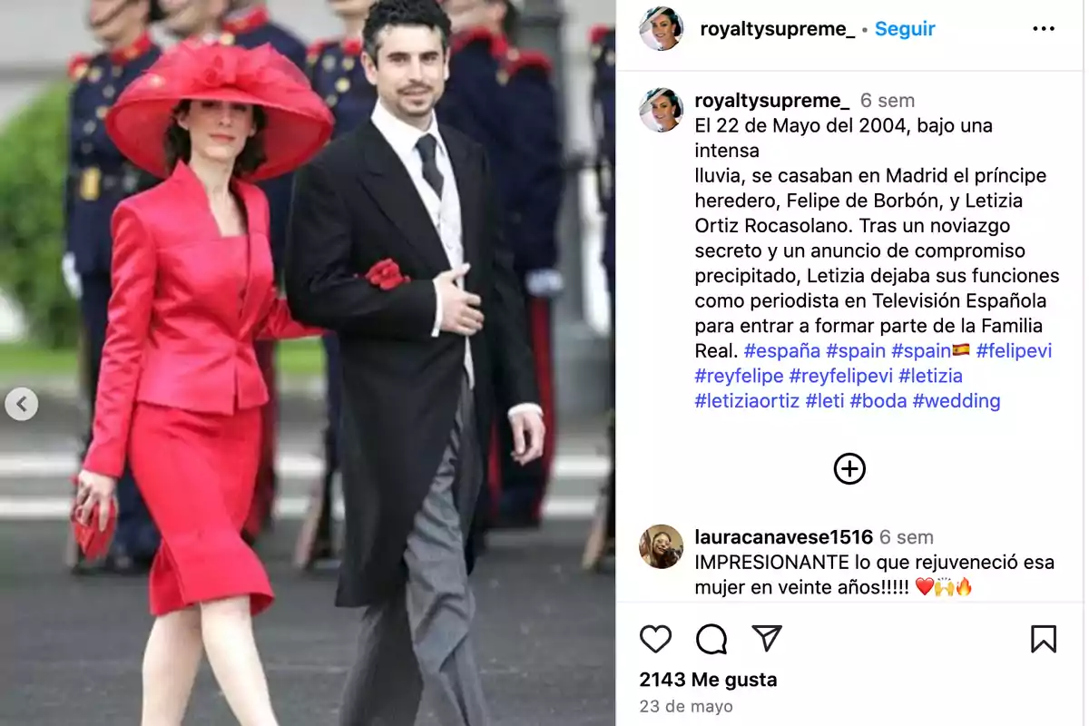 Una mujer vestida con un conjunto rojo y un gran sombrero camina del brazo de un hombre con traje formal, mientras al fondo se ven personas uniformadas. Una mujer vestida con un conjunto rojo y un gran sombrero camina del brazo de un hombre con traje formal, mientras al fondo se ven personas uniformadas.