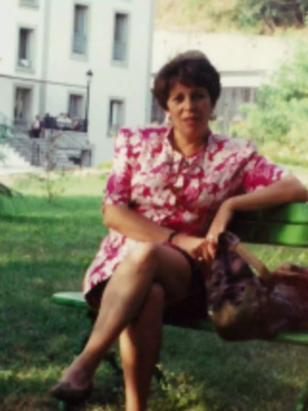 Mujer sentada en una banca verde en un jardín con un edificio al fondo Mujer sentada en una banca verde en un jardín con un edificio al fondo