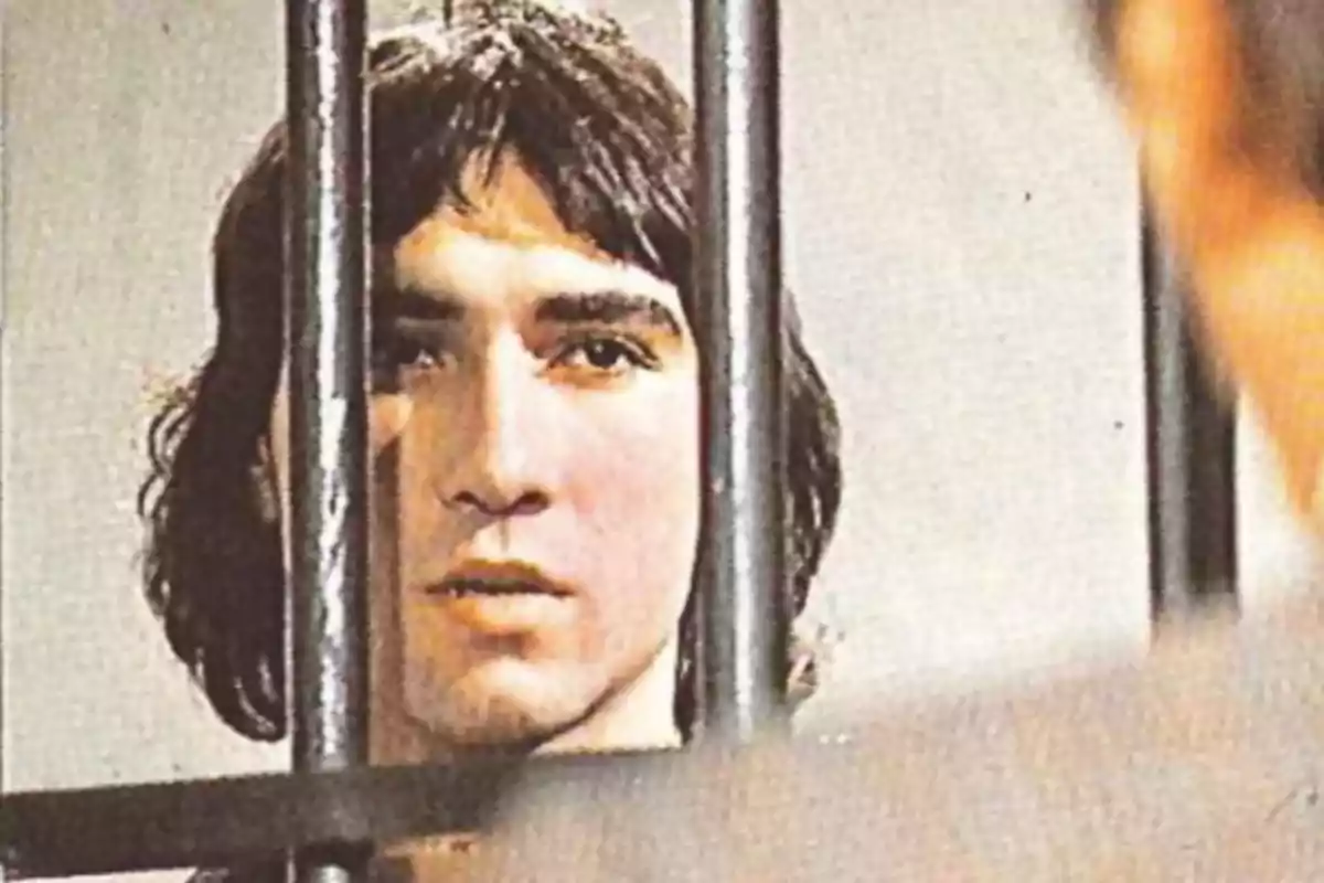 Joven de cabello largo detrás de unos barrotes mirando hacia adelante Joven de cabello largo detrás de unos barrotes mirando hacia adelante