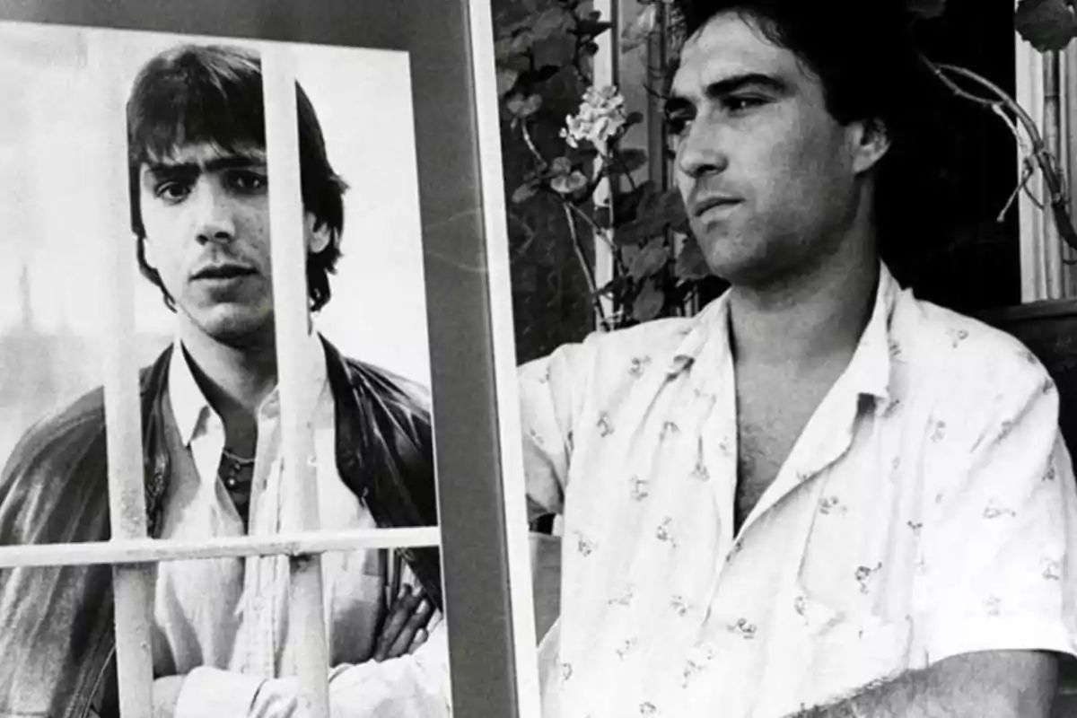 Hombre sosteniendo una fotografía en blanco y negro de sí mismo detrás de unos barrotes Hombre sosteniendo una fotografía en blanco y negro de sí mismo detrás de unos barrotes