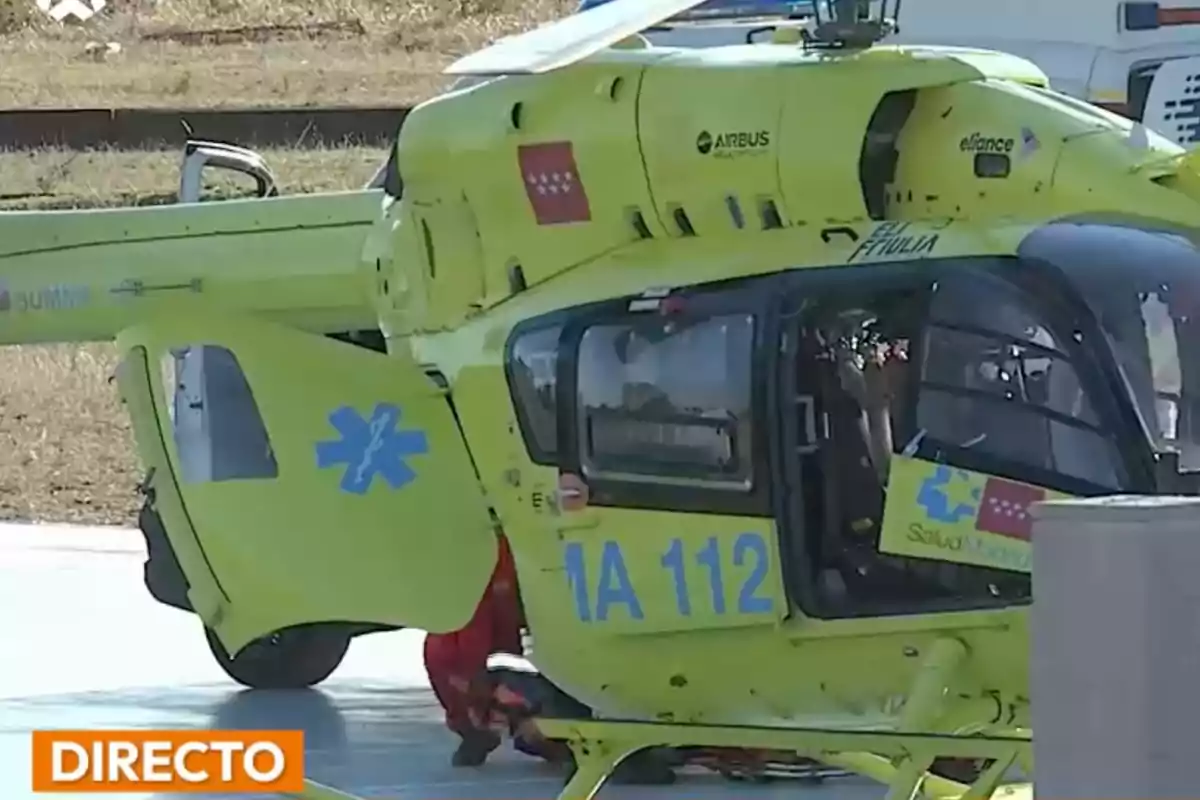 Helicóptero de emergencias médicas amarillo con la puerta abierta y personal sanitario en el suelo Helicóptero de emergencias médicas amarillo con la puerta abierta y personal sanitario en el suelo