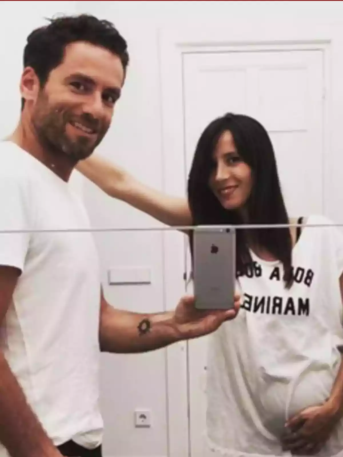 Pareja tomándose una selfie frente a un espejo, la mujer está embarazada y ambos sonríen Pareja tomándose una selfie frente a un espejo, la mujer está embarazada y ambos sonríen