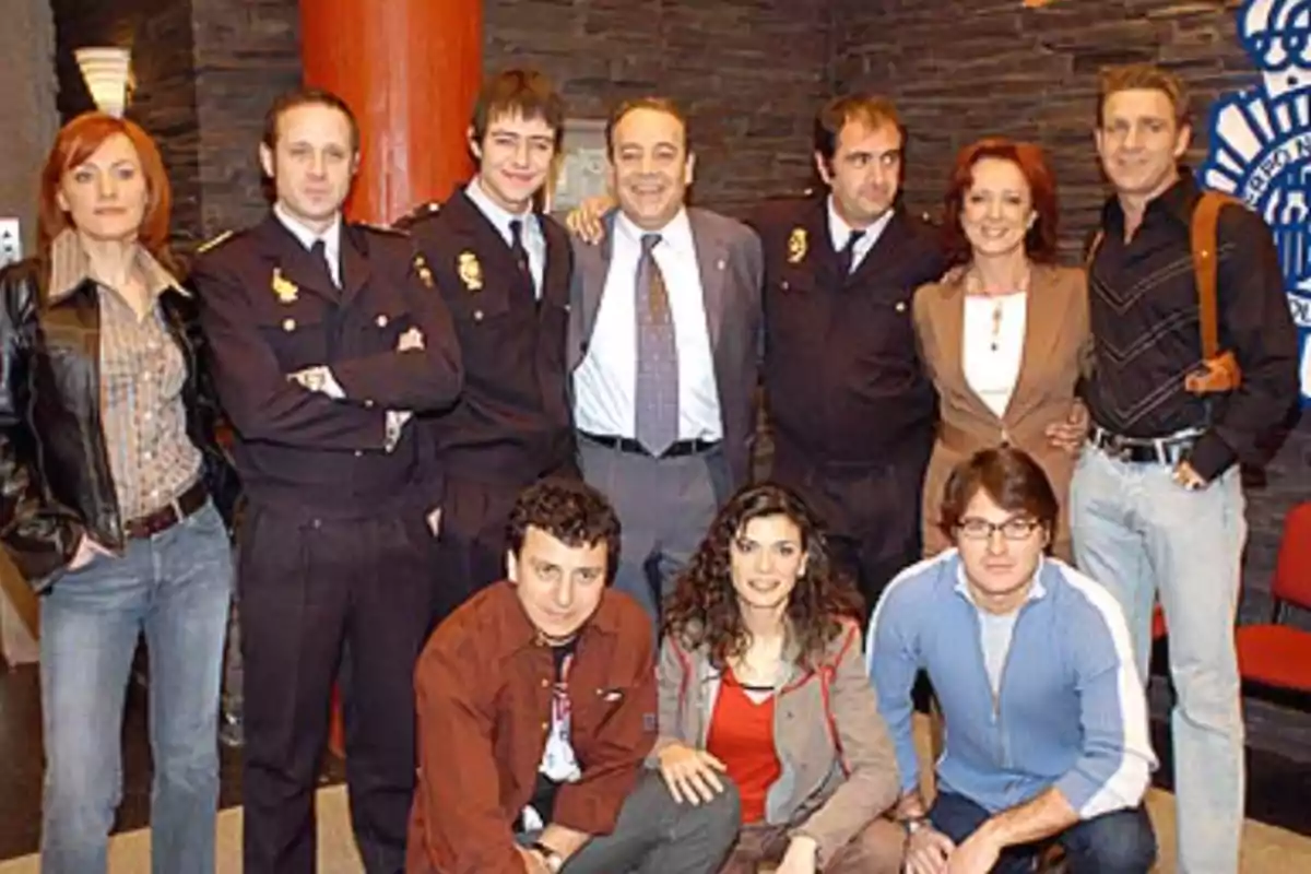 Un grupo de personas posando juntas en un set que parece una comisaría de policía, algunas llevan uniforme y otras ropa casual Un grupo de personas posando juntas en un set que parece una comisaría de policía, algunas llevan uniforme y otras ropa casual